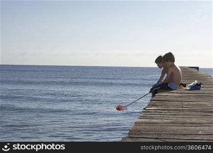 Two boys (6-11) sitting on jetty with fishing net