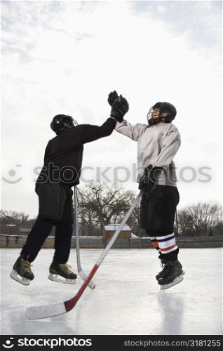 Two boys in ice hockey uniforms giving eachother high five on ice rink.