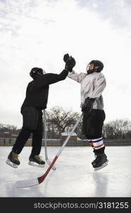 Two boys in ice hockey uniforms giving eachother high five on ice rink.