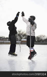 Two boys in ice hockey uniforms giving eachother high five on ice rink.