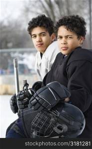 Two boys in ice hockey uniforms sitting on ice rink sidelines looking.