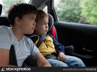 Two boys in the car looking out the window. Little boy sitting in the child safety seat