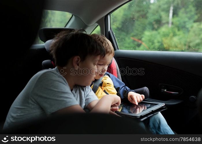 Two boys in the car using a tablet PC, younger boy sitting in the child safety seat