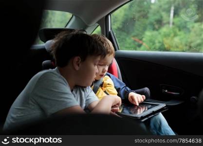 Two boys in the car using a tablet PC, younger boy sitting in the child safety seat