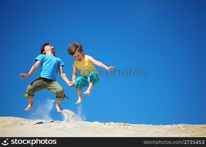 Two boys jump on sand