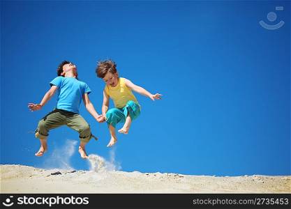 Two boys jump on sand