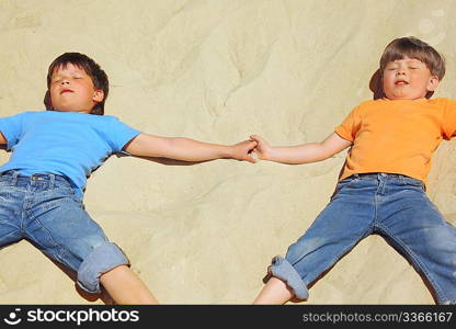 two boys lie on sand with closed eyes