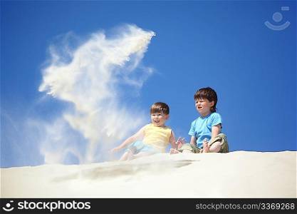 two boys sit on sand and scatter it
