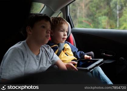 Two boys sitting in the car and looking on the road, little child in child safety seat holding a touchpad