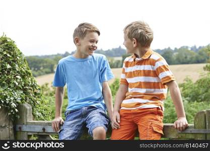 Two Boys Sitting On Gate Chatting Together