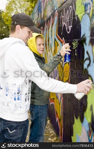Two boys spray painting a stone wall outdoors.