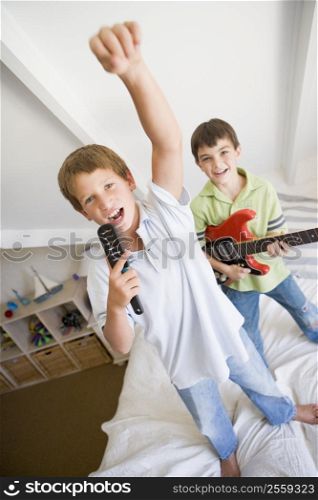 Two Boys Standing On A Bed, Playing Guitar And Singing Into A Hairbrush