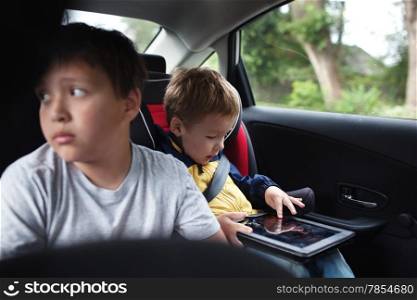 Two boys traveling by car. Elder boy looking out the window, younger one playing with tablet PC