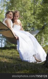two brides romantically involved in hammock against blue sky with forest background