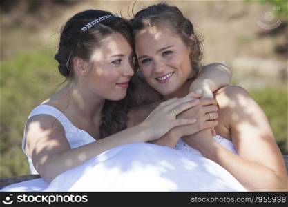 two brides smile and embrace in nature surroundings on sunny day