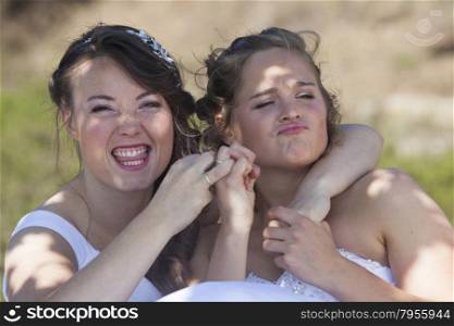 two brides smile and have fun with their wedding rings in nature surroundings on sunny day