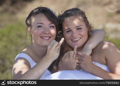 two brides smile and show their wedding rings in nature surroundings on sunny day