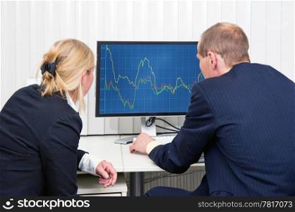 Two brokers analyzing (sales) trends, displayed on a flat screen monitor