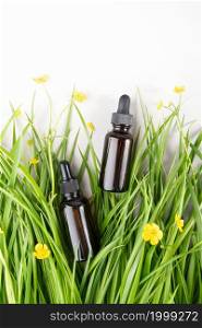 Two brown glass bottles with serum, essential oil collagen or other cosmetic product among the green grass, yellow flowers on white background. Natural Organic Spa Cosmetic concept Mockup.. Two brown glass bottles with serum, essential oil collagen or other cosmetic product among the green grass, yellow flowers on white background. Natural Organic Spa Cosmetic concept Mockup