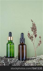 Two brown, green glass bottles with serum, essential oil or other cosmetic product and dry flower plant on tree bark covered with moss against green background. Natural Organic Spa Cosmetic concept.. Two brown, green glass bottles with serum, essential oil or other cosmetic product and dry flower plant on tree bark covered with moss against green background. Natural Organic Spa Cosmetic concept