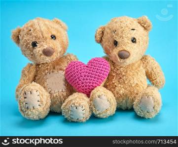 two brown teddy bears hold a red knitted heart on a blue background, love concept