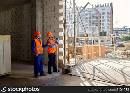 Two builders in uniform standing and talking. Home apartment residential area construction site. Two builders standing and talking about construction