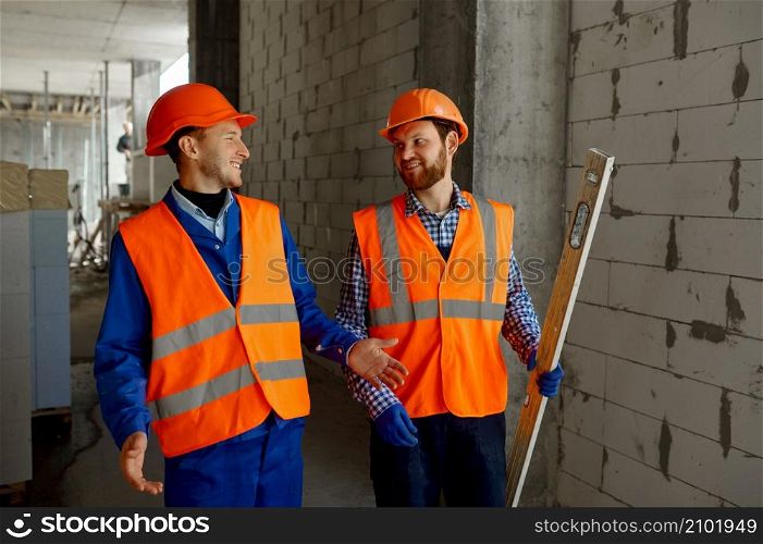 Two builders in uniform walking and talking. Home apartment residential area construction site. Two builders in uniform walking and talking about construction