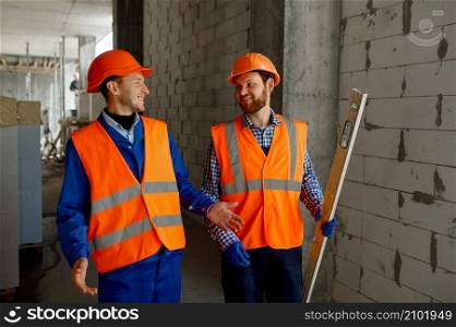 Two builders in uniform walking and talking. Home apartment residential area construction site. Two builders in uniform walking and talking about construction