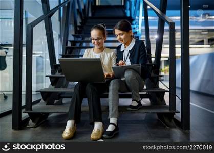 Two business children with laptop and paper document working together sitting on stairs. Two business children working together on stairs
