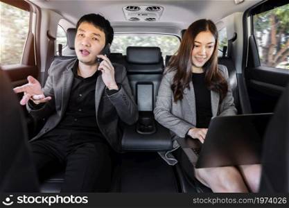 two business man and woman using mobile phone ands laptop computer while sitting at the back seat of a car