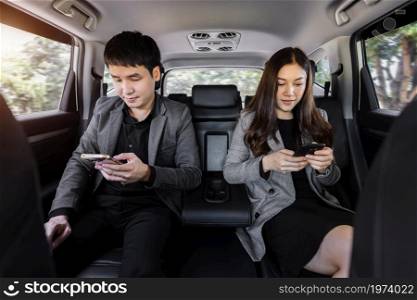 two business man and woman using smartphone while sitting at the back seat of a car