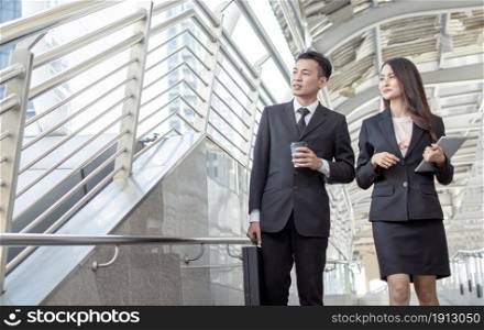 Two business man and woman wearing formal black suits and talking together outside in the morning during going to work