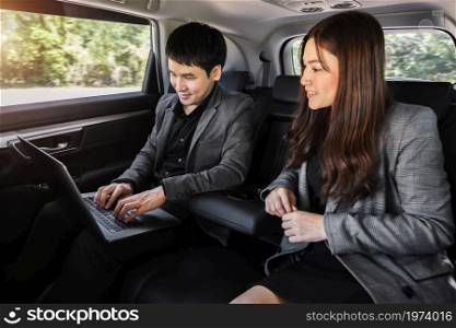 two business man and woman working with laptop computer while sitting in the back seat of a car