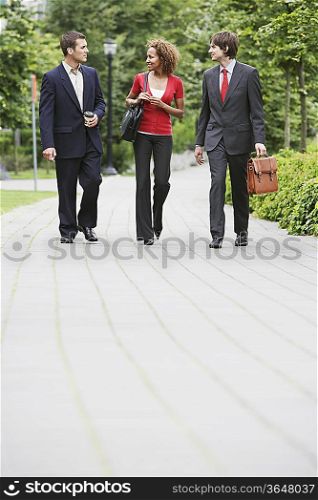Two business men and woman walking through park