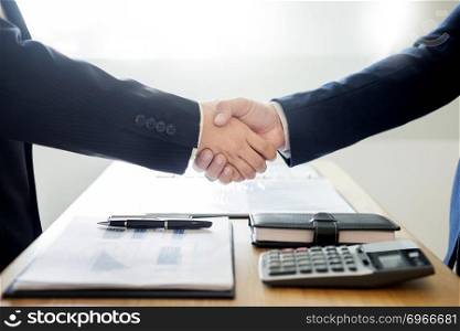 two business men partners shaking hands during a meeting to deal complete to sign agreement contract and become success in the office