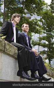 Two business men sitting on wall, outdoors