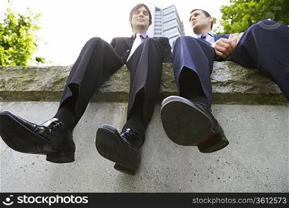 Two business men sitting side by side on wall, low angle view
