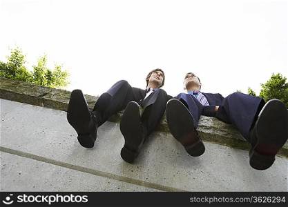 Two business men sitting side by side on wall, low angle view