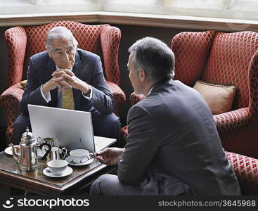 Two business men talking over laptop in lobby
