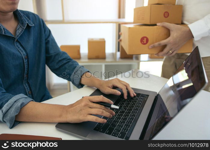 Two business owner are working together to pack products and check customers&rsquo; orders on their laptops at home.