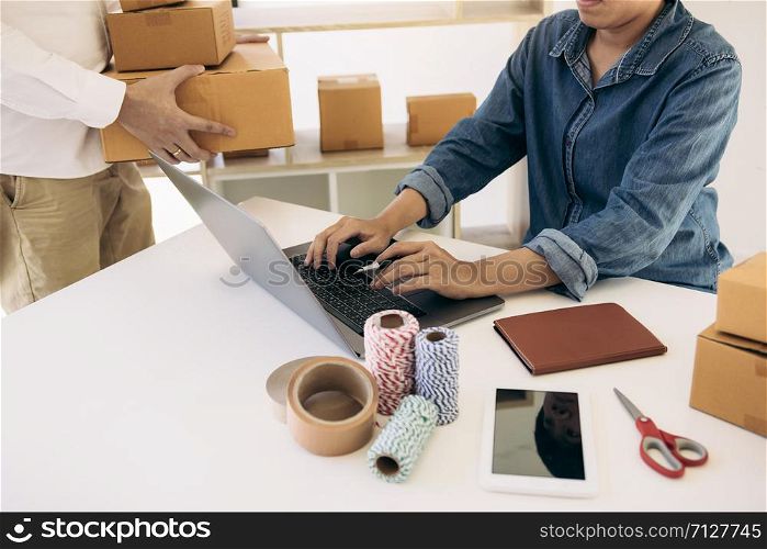 Two business owner are working together to pack products and check customers&rsquo; orders on their laptops at home.