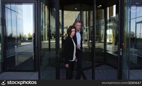 Two business people leaving building through a spinning door and talking