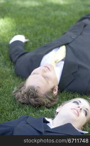 Two business people lying down in the grass in the park taking a break and smiling