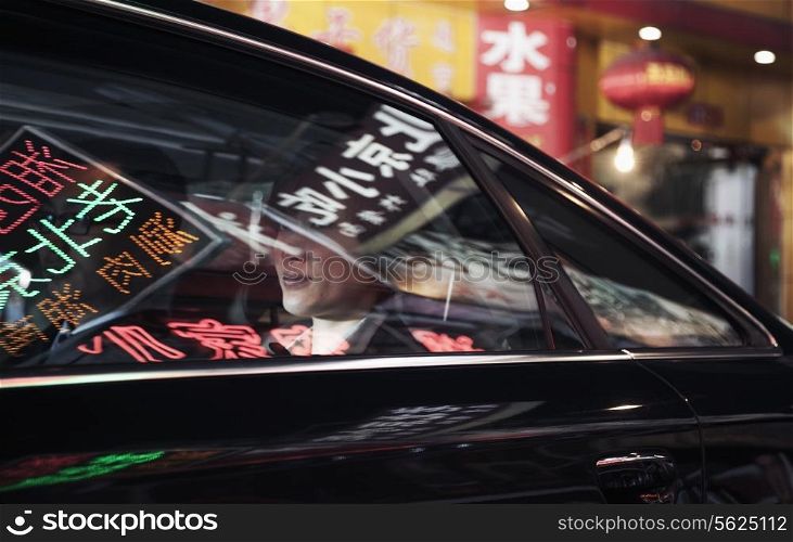 Two business people sitting in the back of a car driving through the city at night, reflections of store signs on the car