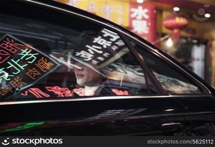 Two business people sitting in the back of a car driving through the city at night, reflections of store signs on the car