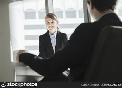 Two business people sitting, smiling and looking at each other during a business meeting