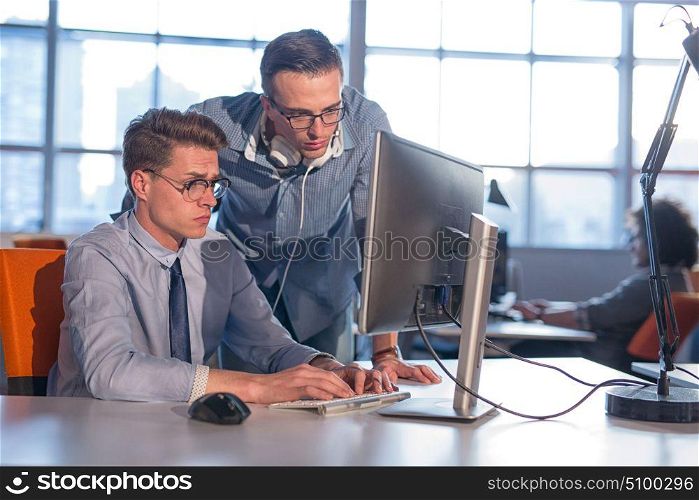 two business people using computer preparing for next meeting and discussing ideas with colleagues in the background