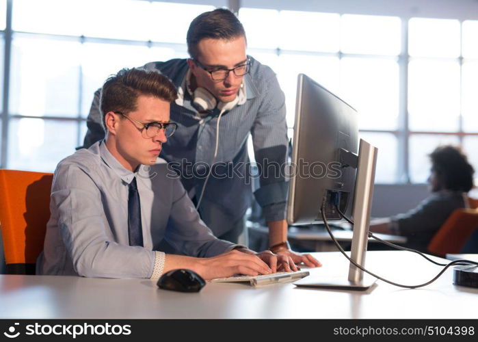 two business people using computer preparing for next meeting and discussing ideas with colleagues in the background