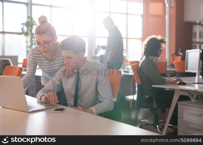 two business people using laptop preparing for next meeting and discussing ideas with colleagues in the background