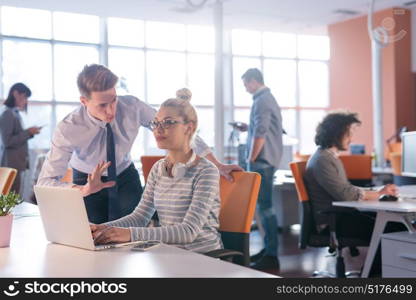 two business people using laptop preparing for next meeting and discussing ideas with colleagues in the background